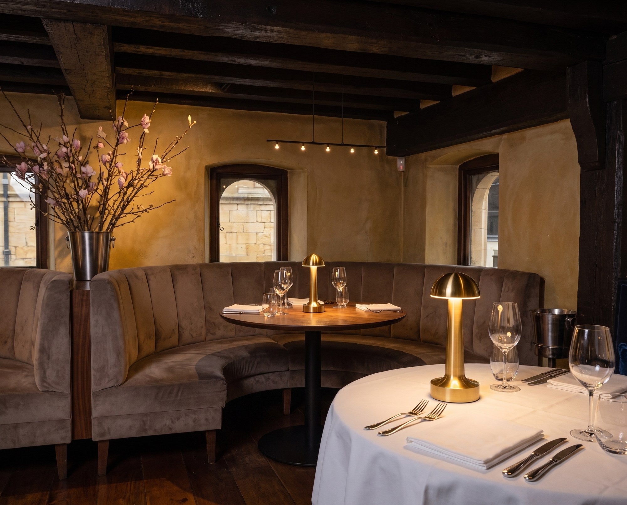 Two Aveline lamps lit on set tables in a beamed dining room