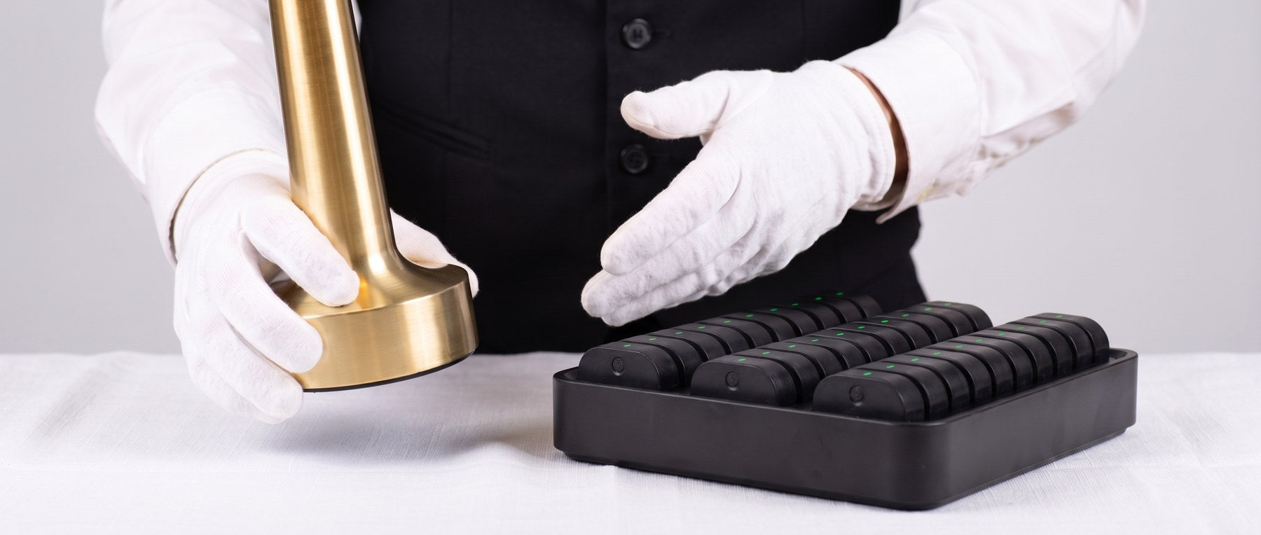 A gloved waiter setting a brass lamp down beside a charging station of ready batteries.