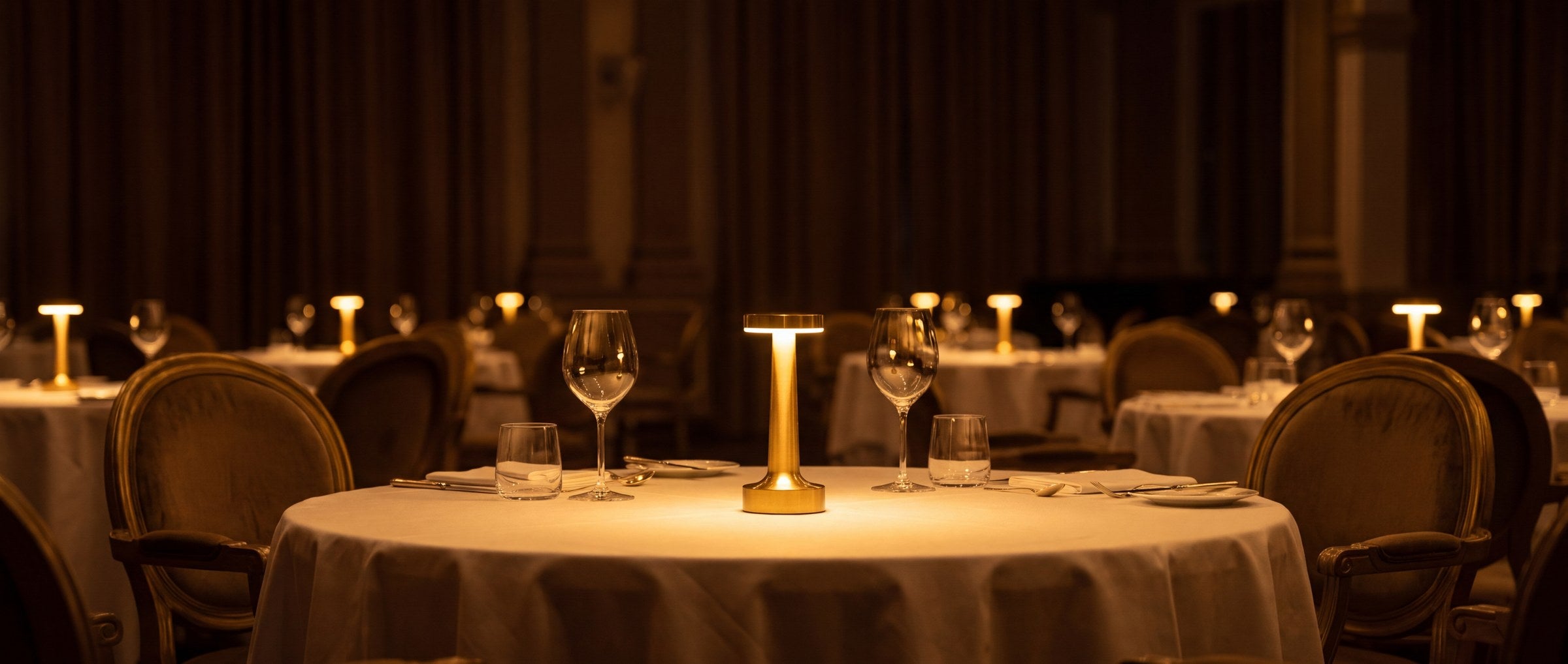 A dressed table lit by a brass Clarté lamp, with more lit tables receding into the room.