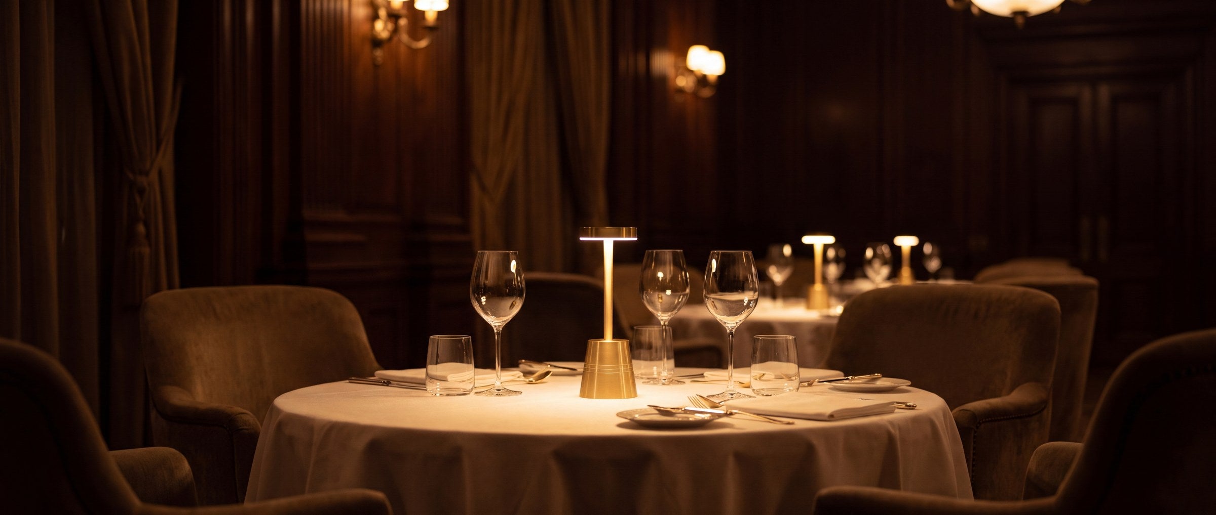 A dressed table in a panelled dining room, lit by a single brass Clarté lamp.