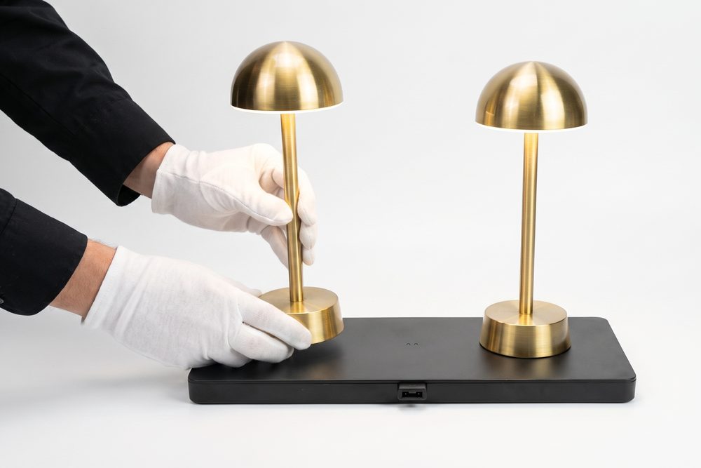 Two lamps standing on a charging dock, one being set down by a gloved hand