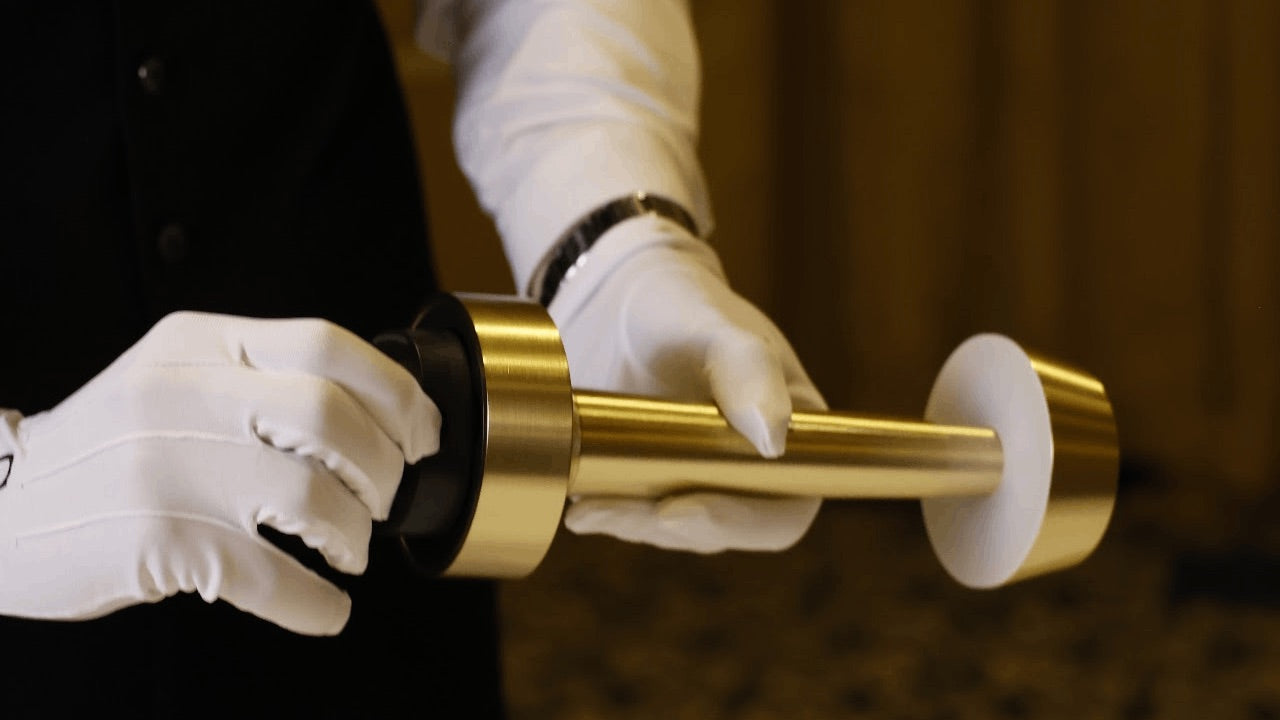 Two gloved hands separating the battery from a brass Clarté lamp.