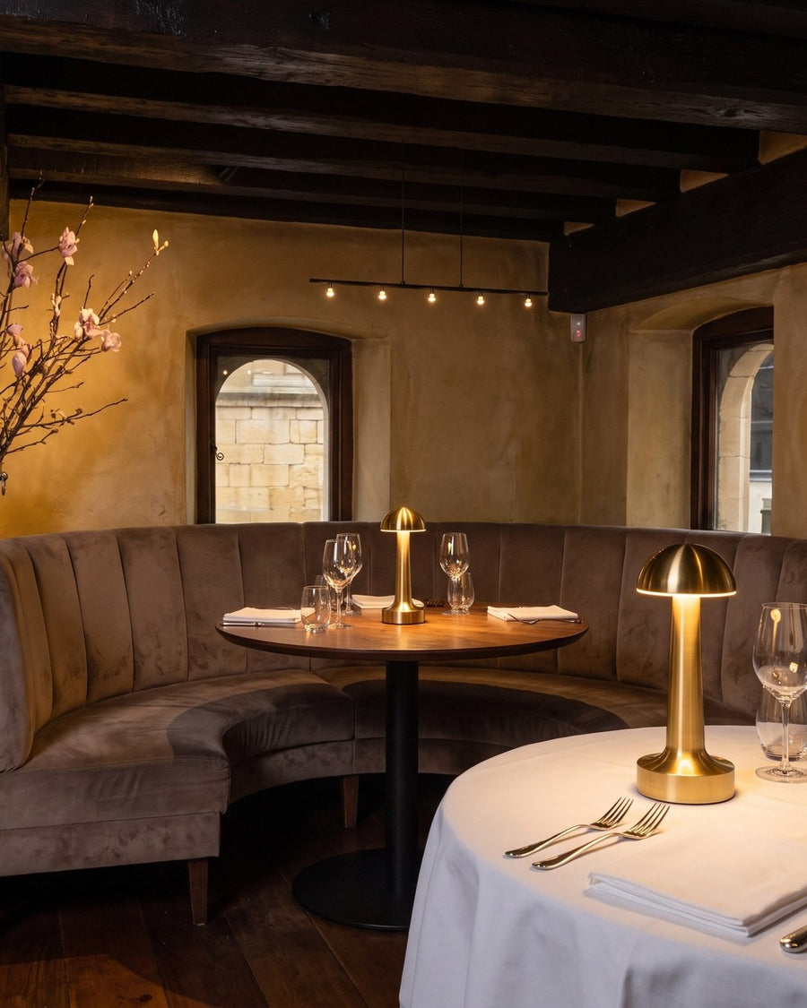Clarté lamps on tables in a beamed dining room with stone windows