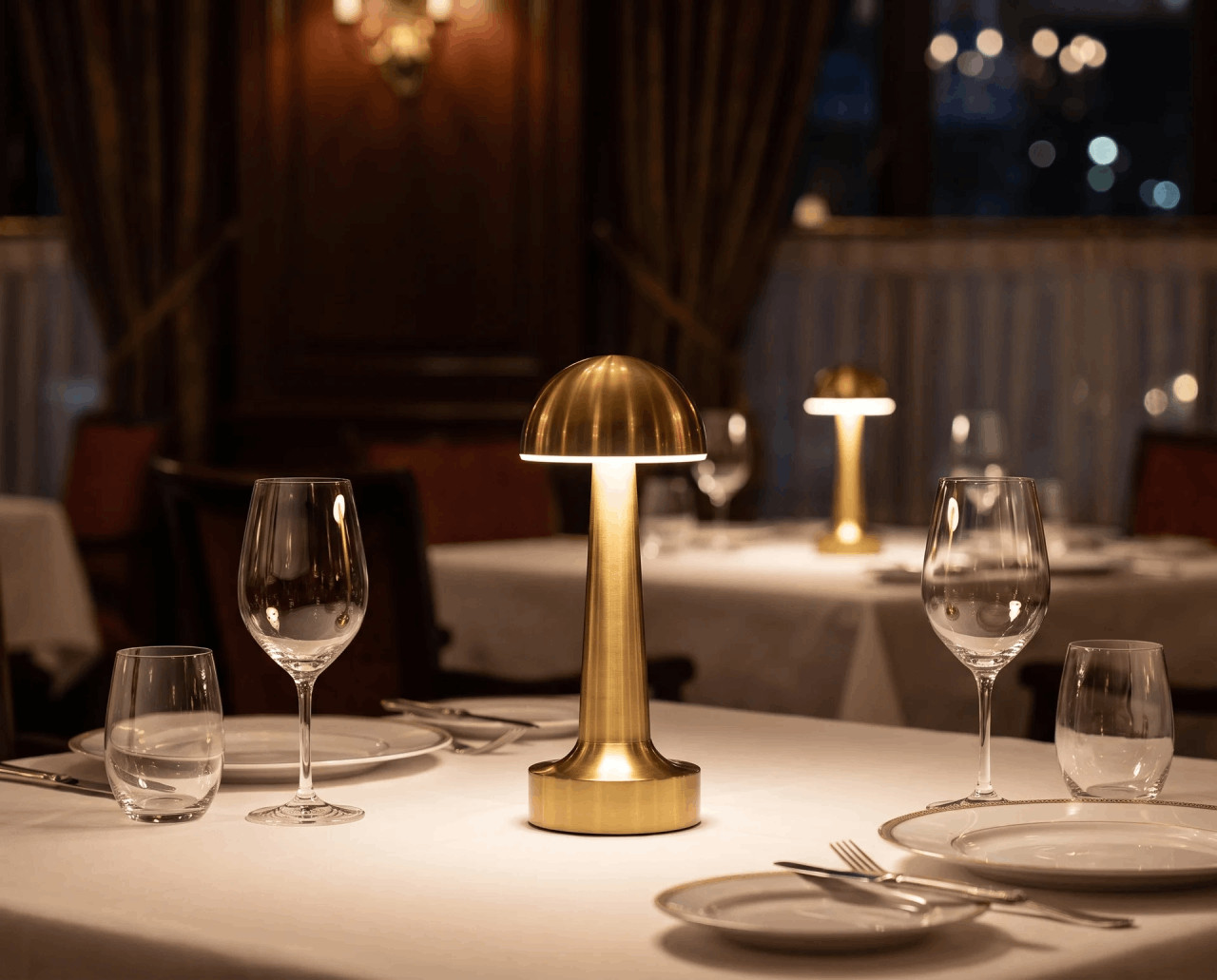 A cordless brass lamp lighting a set dinner table in a warm restaurant